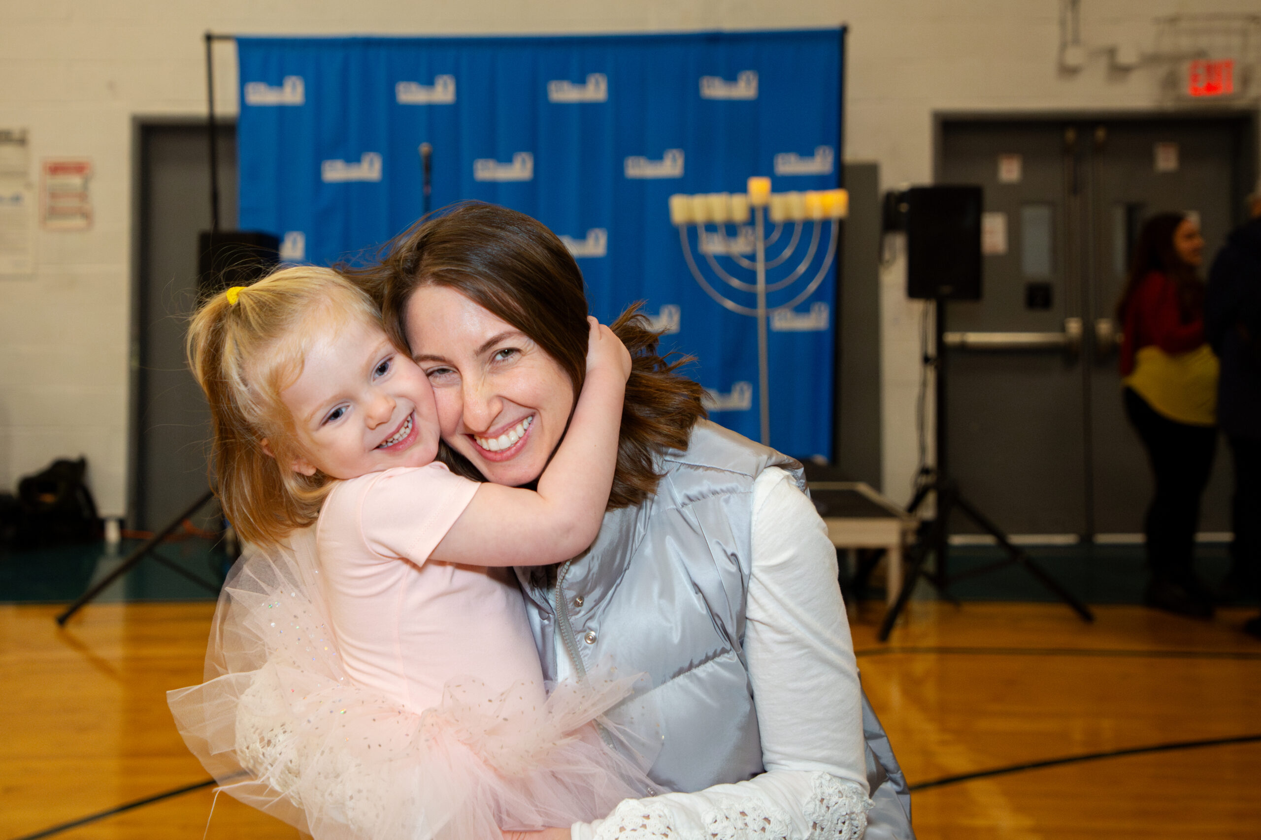 Female senior citizen holding a loaf of bread while being surrounded by a diverse group of people smiling happily with one another.