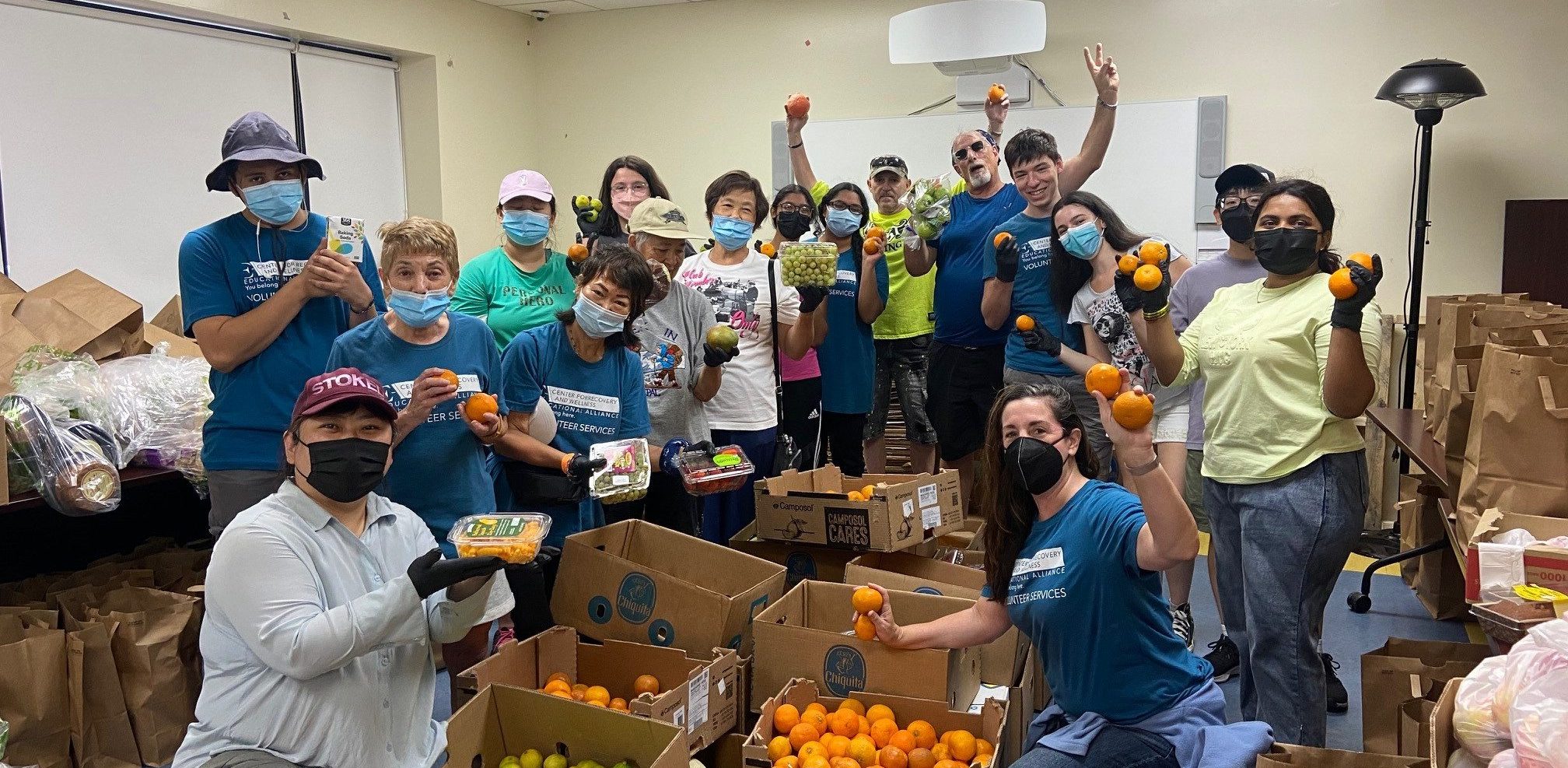 Group of people standing around fruit and fruit boxes inside celebrating